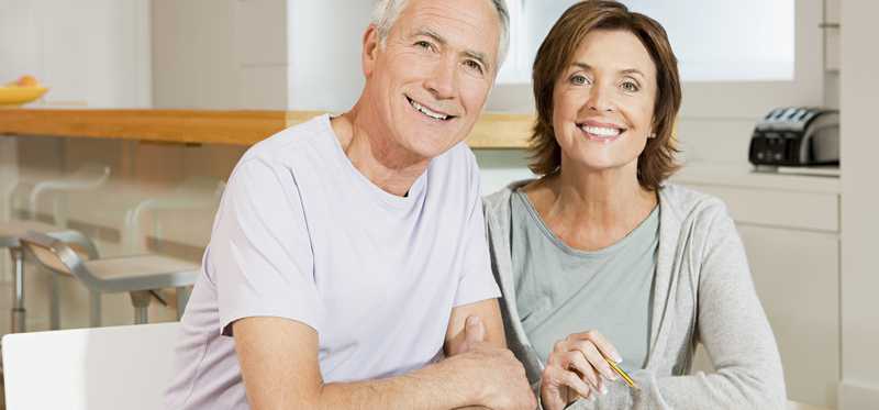 A smiling mature couple sitting at a table with a calculator while discussing their finances.