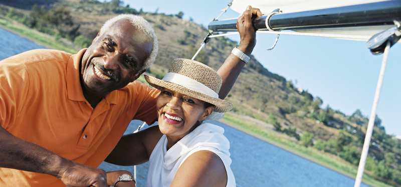 A smiling senior couple holding hands as they sail on the water.