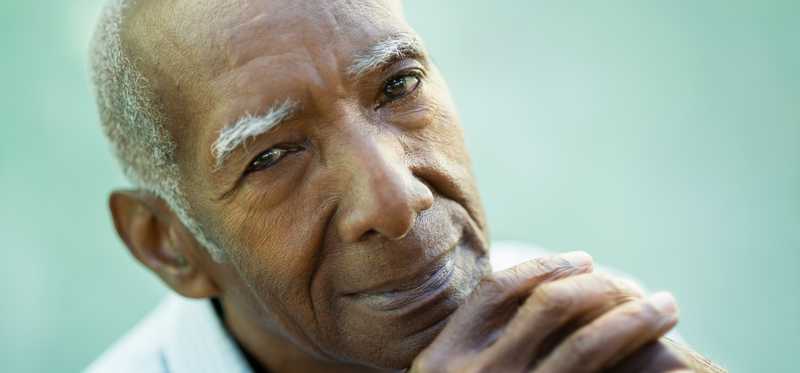 A smiling senior man with his hands interlocked in front of his chin.