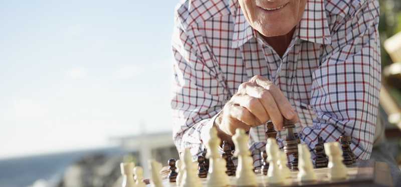 A smiling person playing chess near the beach.