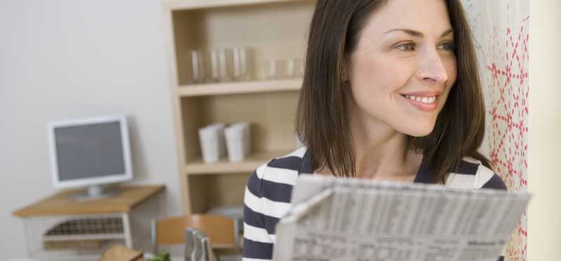 A smiling woman holding a financial newspaper while looking off into the distance.