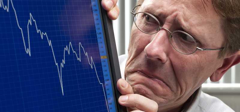 A worried man looking at a plunging stock chart on a computer monitor.