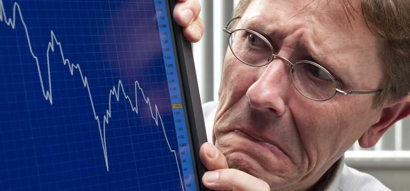 A worried man looking at a plunging stock chart on his computer monitor.
