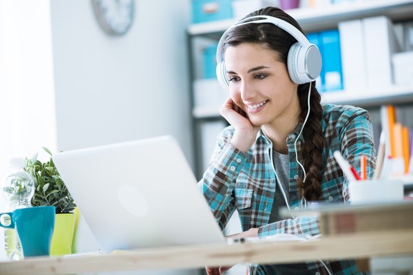 A young woman with headphones on listens to music on her laptop.