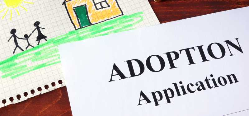 Paperwork reading Adoption Application next to a child's drawing.