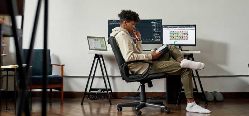 Person looks at book while sitting at computer.