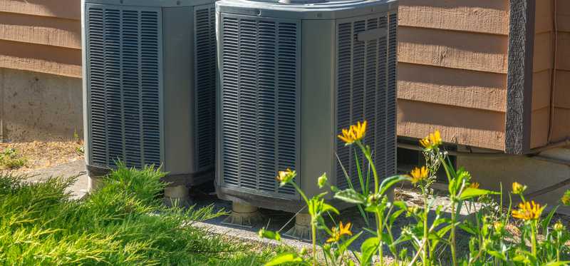 Two air conditioner units side by side outside of a home.