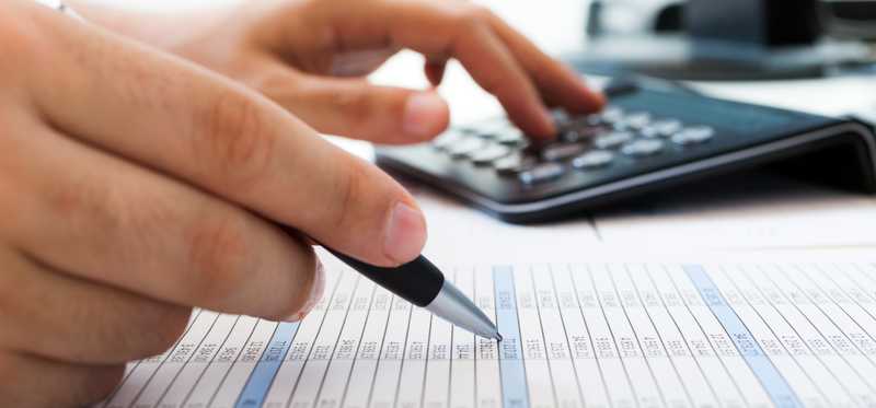An accountant checking a report line by line with the aid of a calculator.