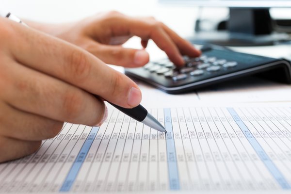 An accountant checking a report line by line with the aid of a calculator.