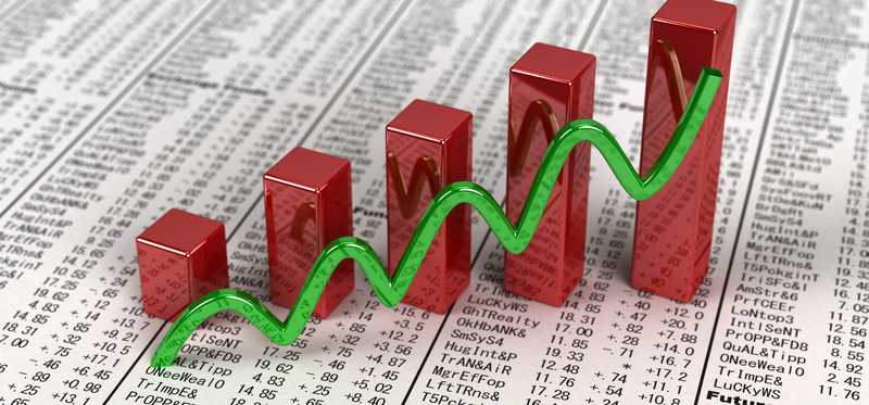 An ascending green line and bar chart on a financial newspaper with stock quotes