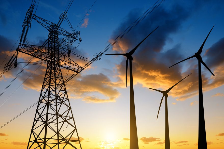 An electrical grid next to three wind turbines at sunset.