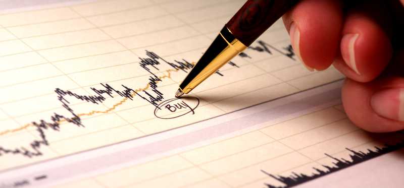 An investor writing and circling the word buy underneath a dip in a stock chart.