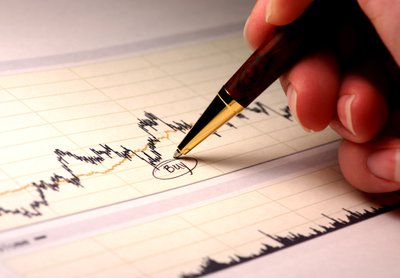 An investor writing and circling the word buy underneath a dip in a stock chart.