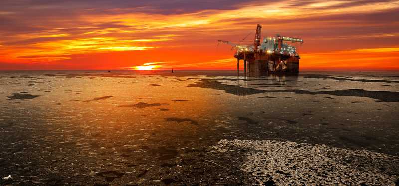 An offshore oil rig platform with the sun rising on a frozen sea.