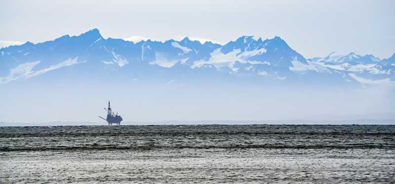 An oil platform in the icy waters off Alaska with snow-capped mountains in the background.