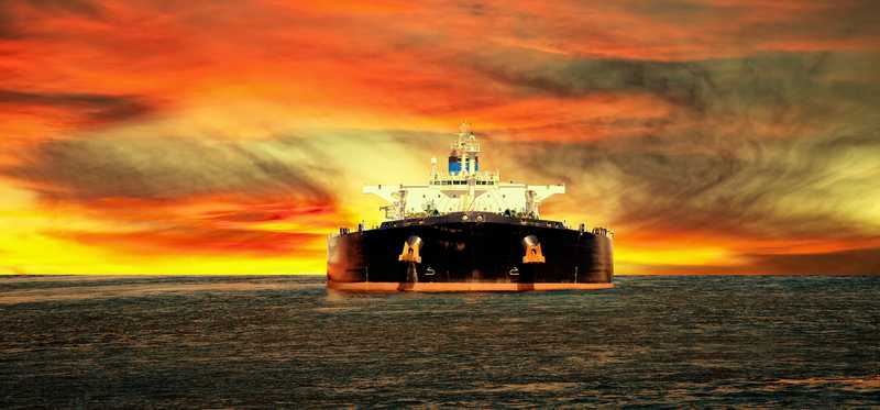 An oil tanker ship at sea with a sunset sky in the background.