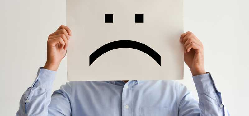 A man holds a paper angry face over his face.