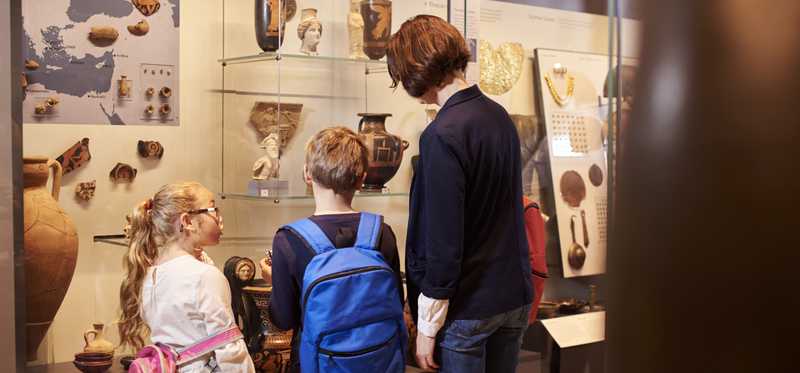 Adult and two children look at artifacts on display in a museum.
