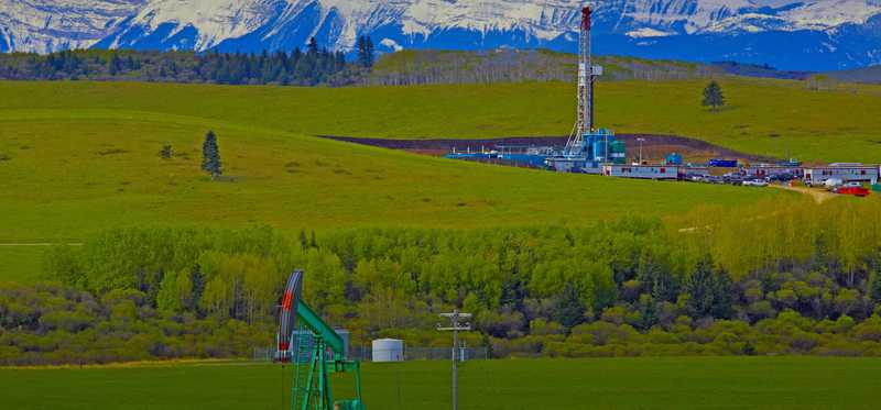 A drilling rig and pump jack with mountains in background.
