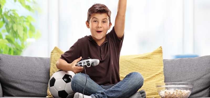 A boy on a couch with his hand raised in victory while playing video games.