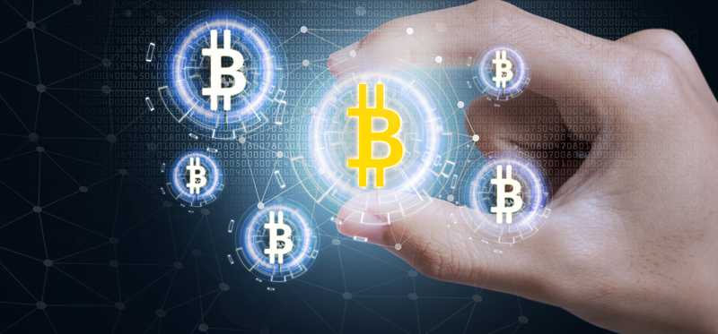 Gold bitcoin symbol held between fingers.