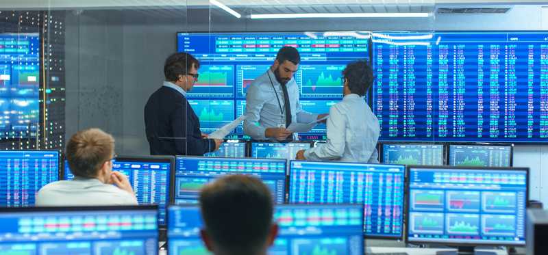 A room full of monitors with stock prices displayed and stockbrokers working.