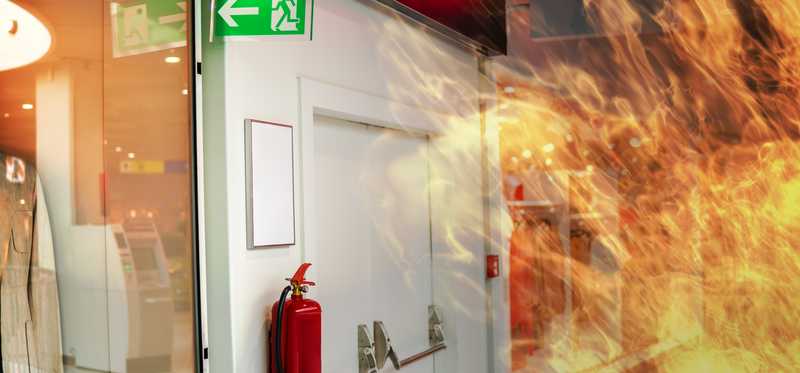 A fire in a warehouse next to an emergency sign and fire extinguisher.
