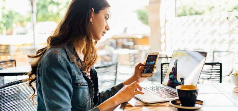 Person looking at laptop and phone in an outdoor cafe.