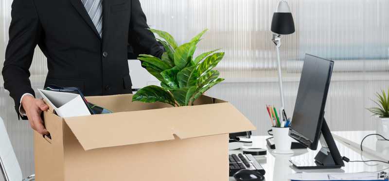 Businessperson carrying cardboard box in office.