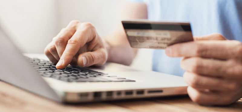 A person at a laptop holds a credit card.