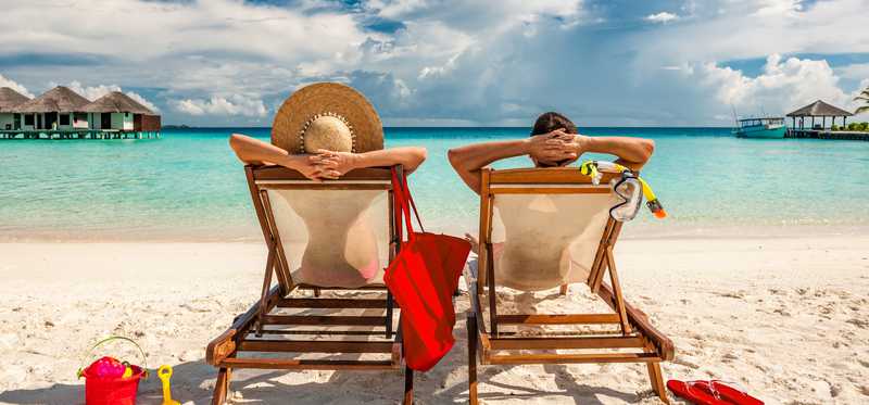 Two people sitting in lounge chairs on the beach.