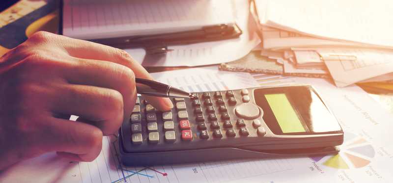 A hand using a calculator on a desk filled with paperwork