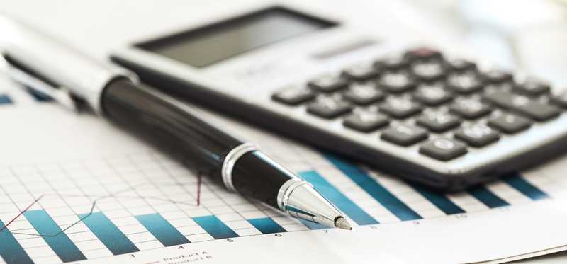 A calculator and pen sit atop some graphs on paper.
