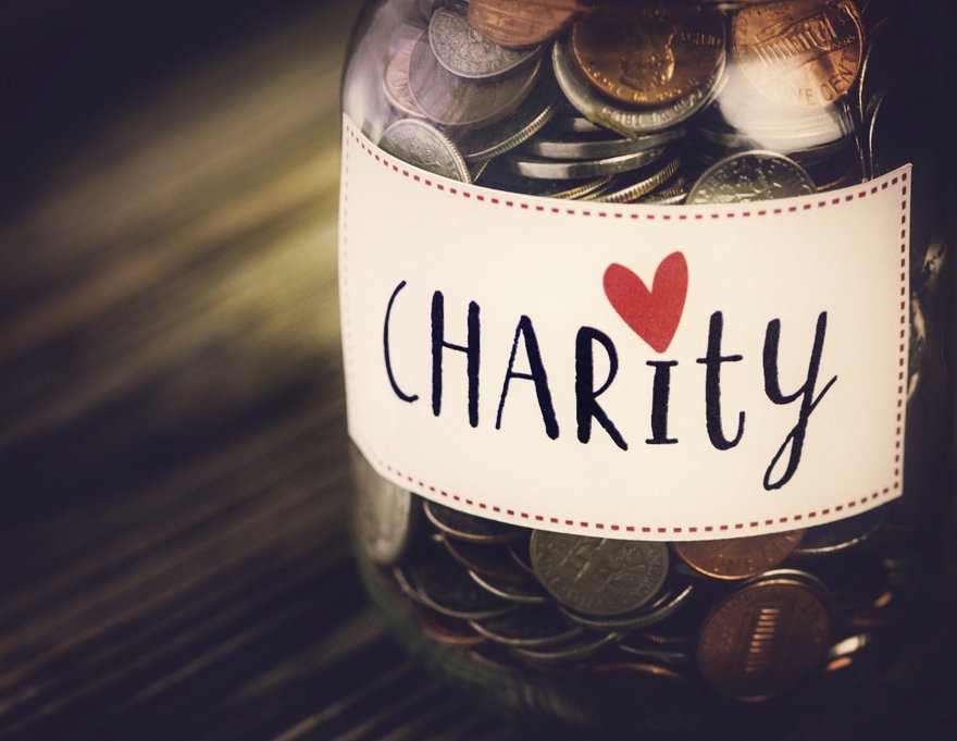 Glass jar filled with coins is labeled Charity.