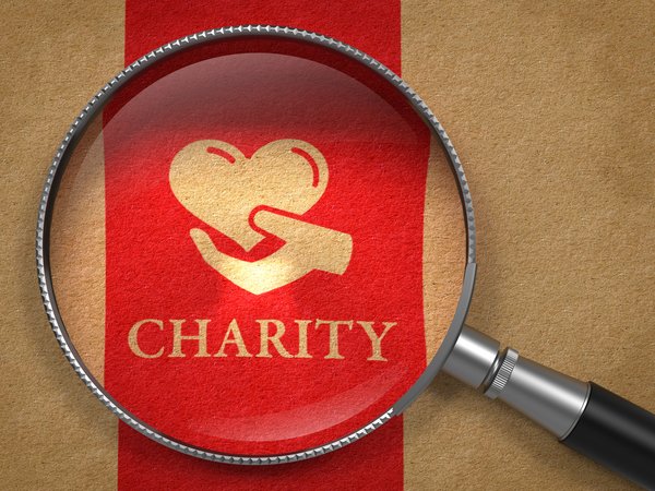 The word Charity with a hand and red ribbon under a magnifying glass.