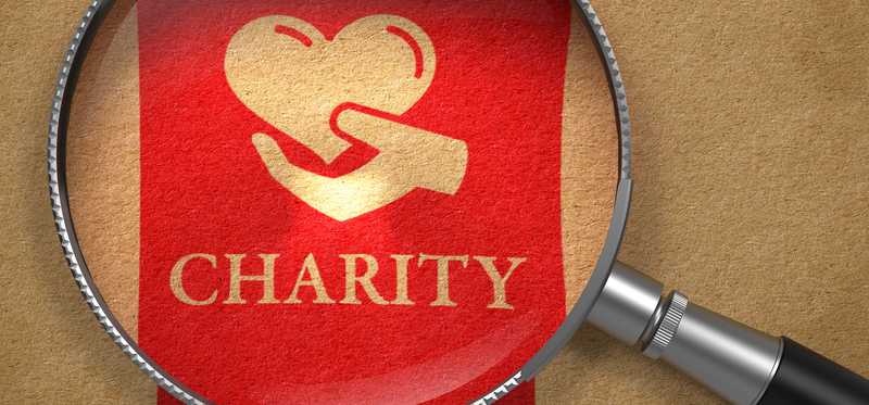 Magnifying glass over red ribbon reading Charity.