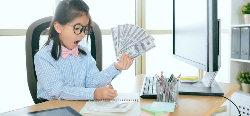 Child in glasses at desk with cash and surprised look on her face