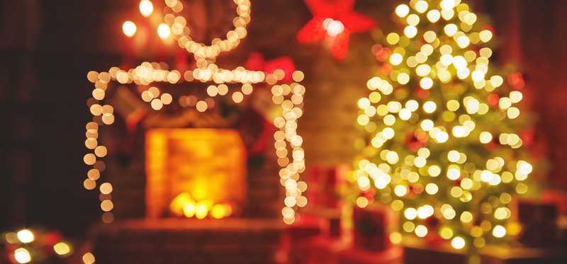 A Christmas tree and other decorations by a fireplace in a dimly lit room.