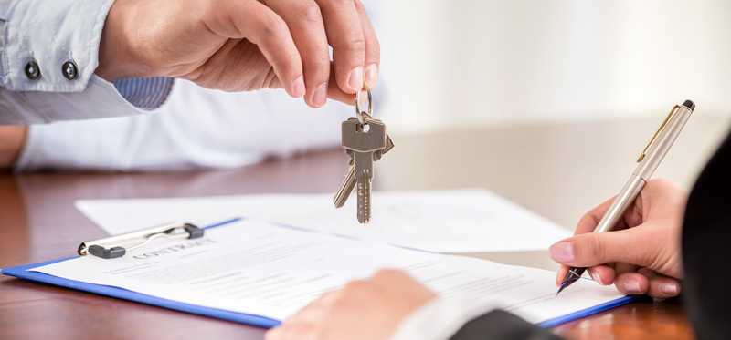 A person hands house keys to another person at a real estate closing.