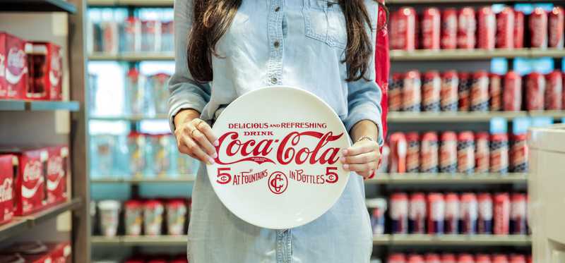Person holding a Coca-Cola plate inside a Coke store.