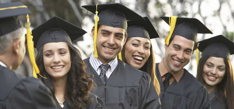 A group of college graduates stands in a line in black gowns.