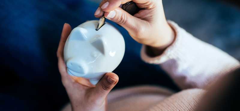 Person placing coin in white porcelain piggy bank