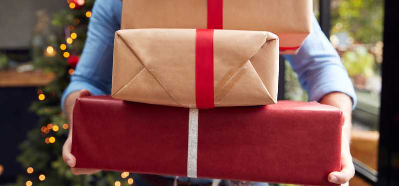 Person carrying large stack of Christmas gift boxes