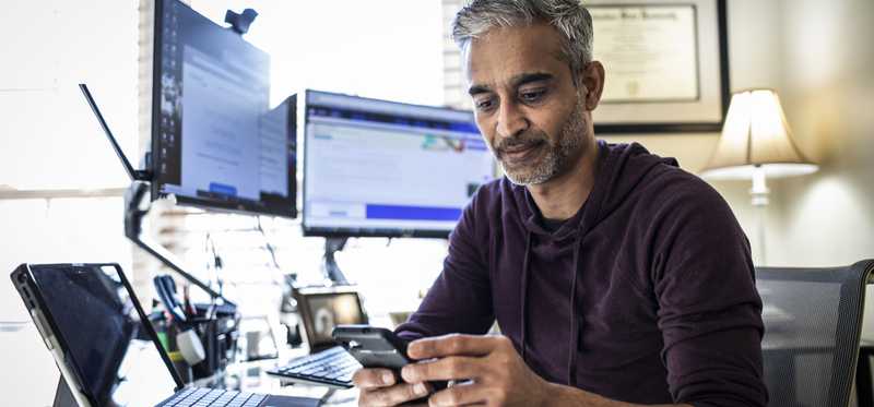 Man sitting at desk with dual monitors and looking at phone