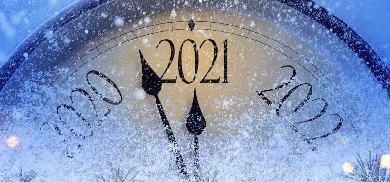 Snowflakes partially covering yearly clock with the hands almost touching 2021