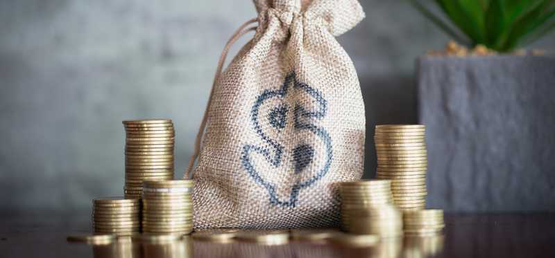 Stacks of coins next to a burlap bag with dollar sign.