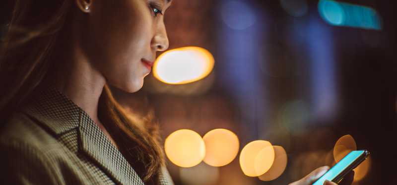 Person looking at phone against lit background.
