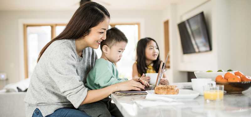 Mother looking at laptop while sitting at kitchen island with children
