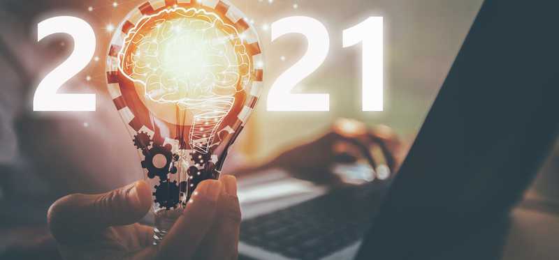 Light bulb illuminated over background of person on laptop and illuminated 2021 sign