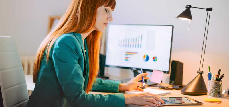 Red haired woman sitting at desk with computer while reviewing financial charts